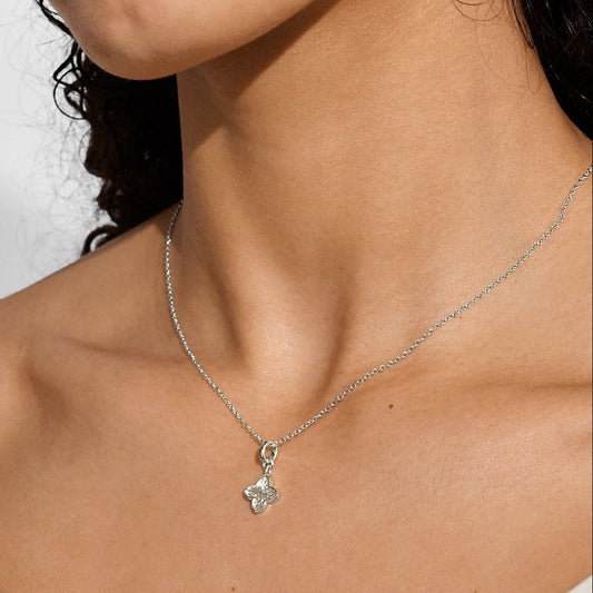 Silver necklace with a textured clover pendant worn by a person