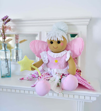 Toy fairy with pink wings and dress sitting on a white surface.