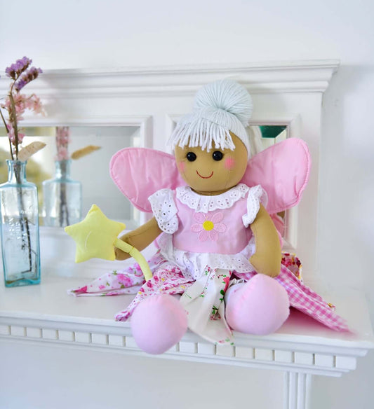 Toy fairy with pink wings and dress sitting on a white surface.